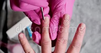 美甲师傅在粉红色手套上用电钻刮掉美甲沙龙的旧清漆。 美容专业美甲